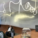 Curved LED light line on the ceiling above a seating area with two people....