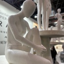 A mannequin sitting in the foreground with one leg bent, wearing no clothes...