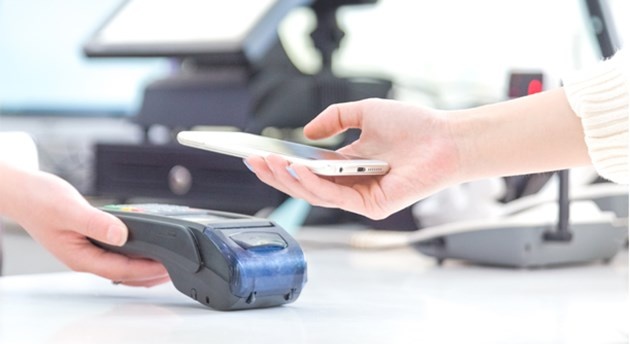 a smartphone holding in the hand is placed over an NFC reader to make a payment...