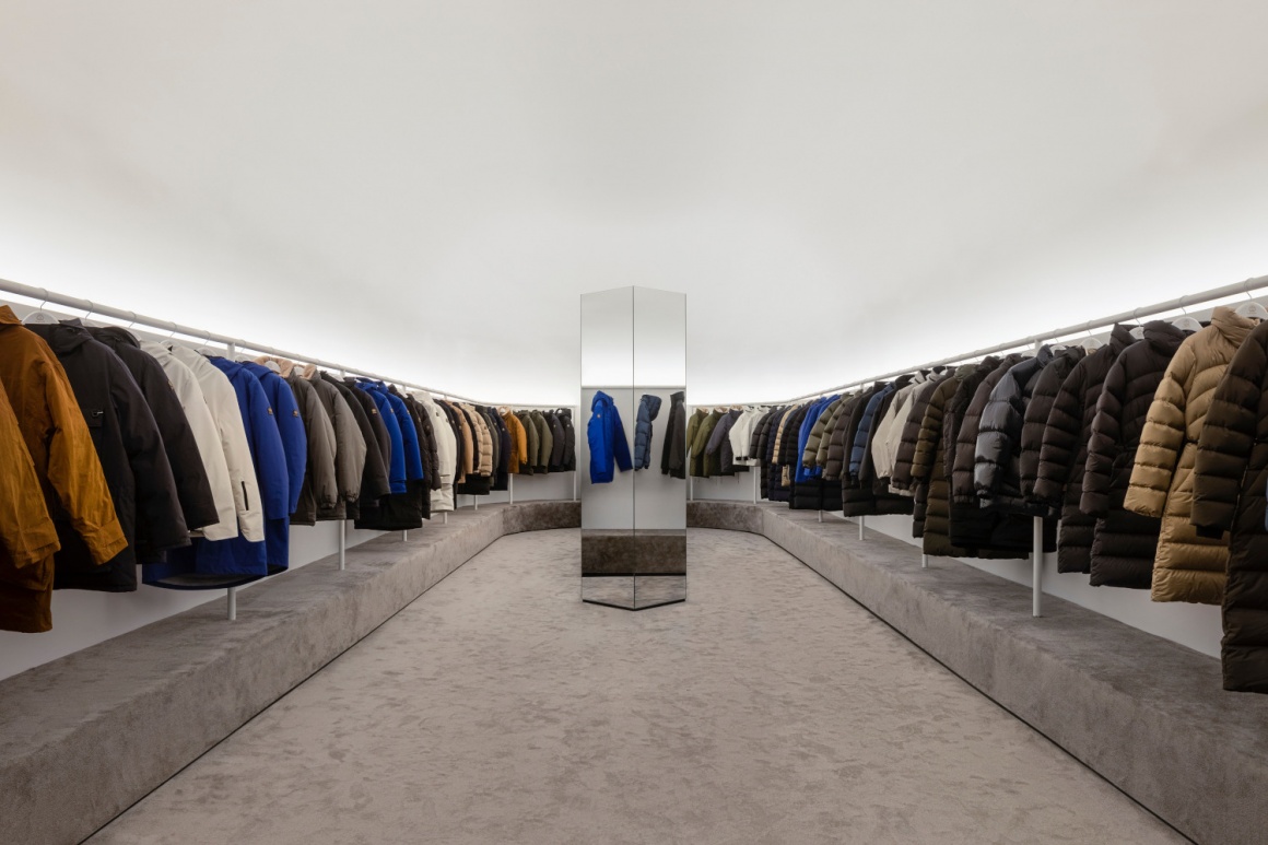 A fashion store selling coates with coat racks left and right and a mirror...