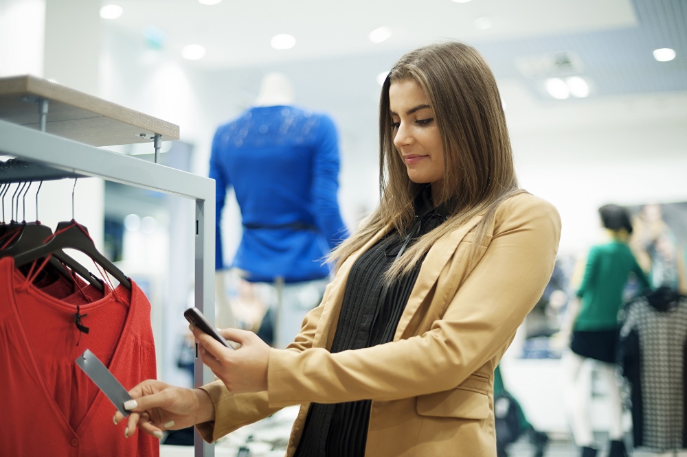 A woman in a fashion store scans a clothing tag with a smartphone; copyright:...