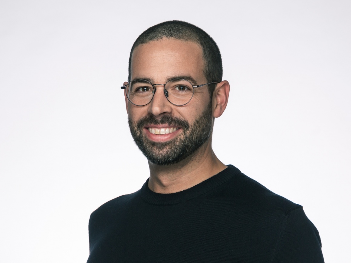 A man with glasses and in black shirt smiles at the camera...