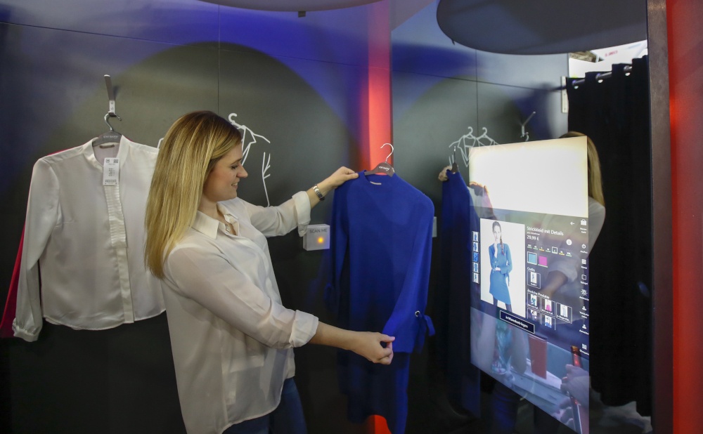A young woman looks at a blouse in a dressing room, with an interactive digital...