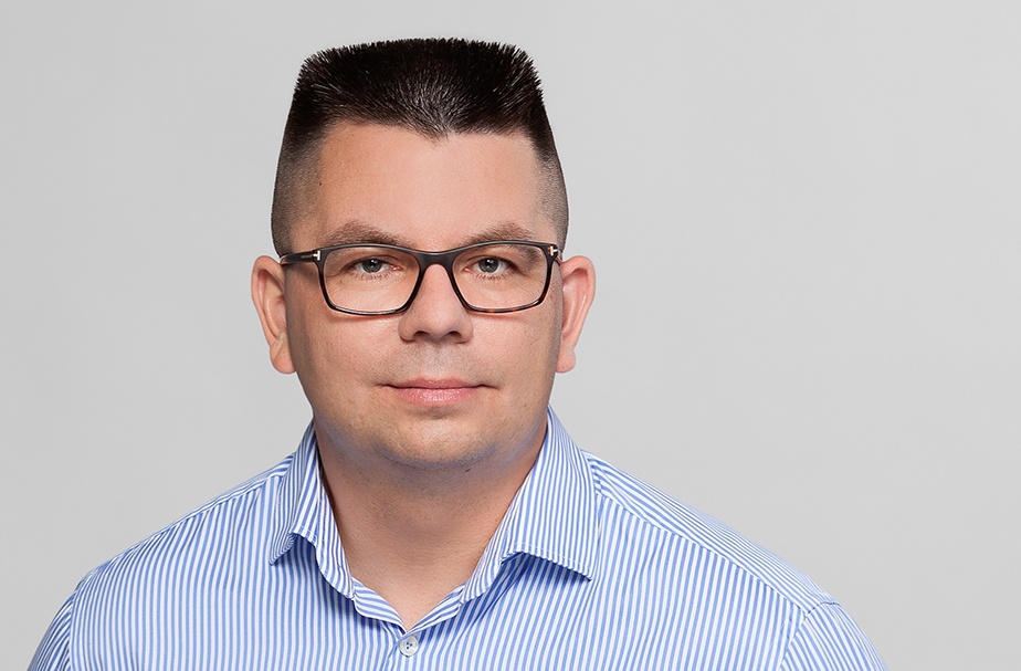 Man in blue shirt with glasses and short hair looks at camera...