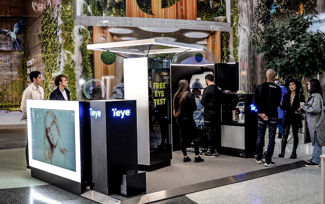 A kiosk for eye testing with people milling around; copyright: ieye...