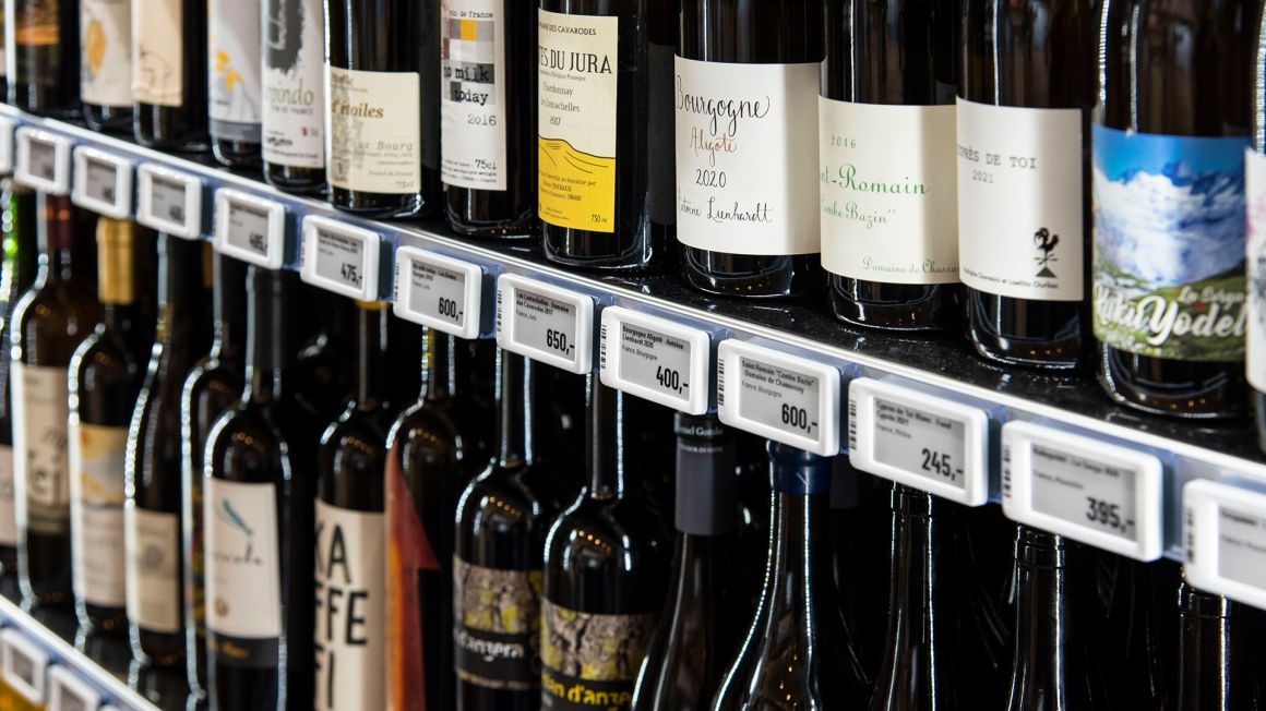 Various bottles of wine are placed on a shelf with electronic shelf labels....