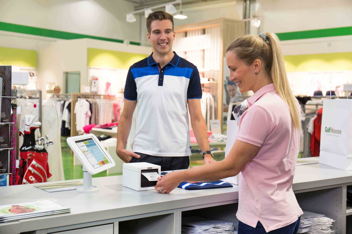 A smiling cashier takes a receipt from a checkout printer, with a smiling...