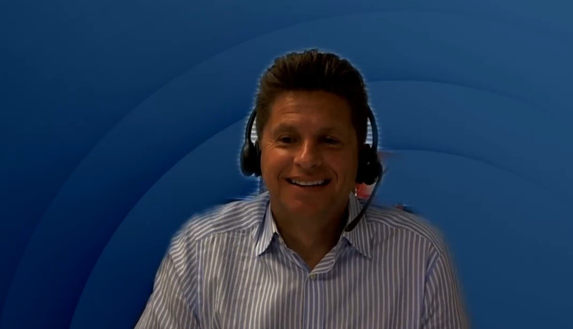 A man with headphones and microphone at a webtalk infront of a blue background...