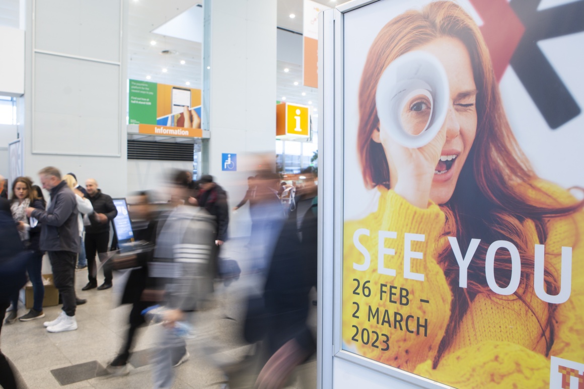 A poster at EuroShop 2020 announces EuroShop 2023. Visitors walk behind it....