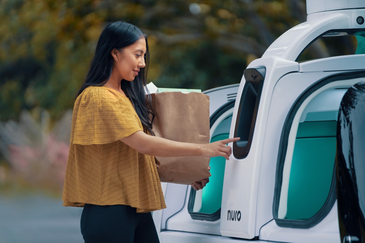 A person is taking a bag with groceries out of an autonomous vehicle by Nuro...
