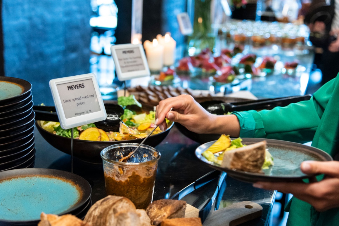 A person takes something from a buffet. Two digital buffet signs can be seen....