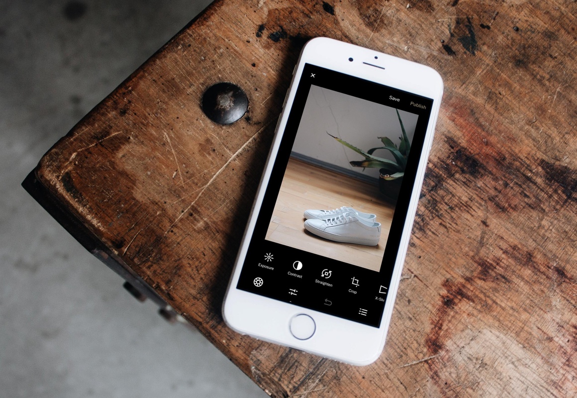 A cell phone on a wooden table with a picture of white shoes on it...