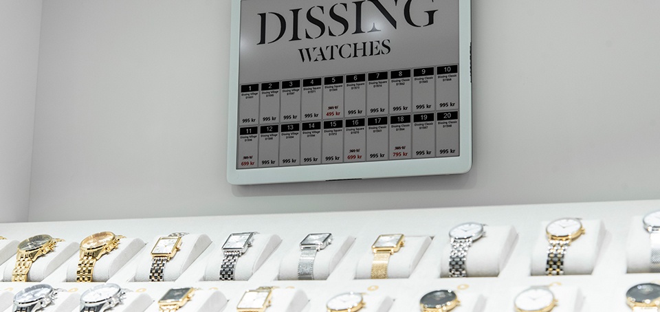 A selection of high-quality watches. A large digital price tag hangs above it....