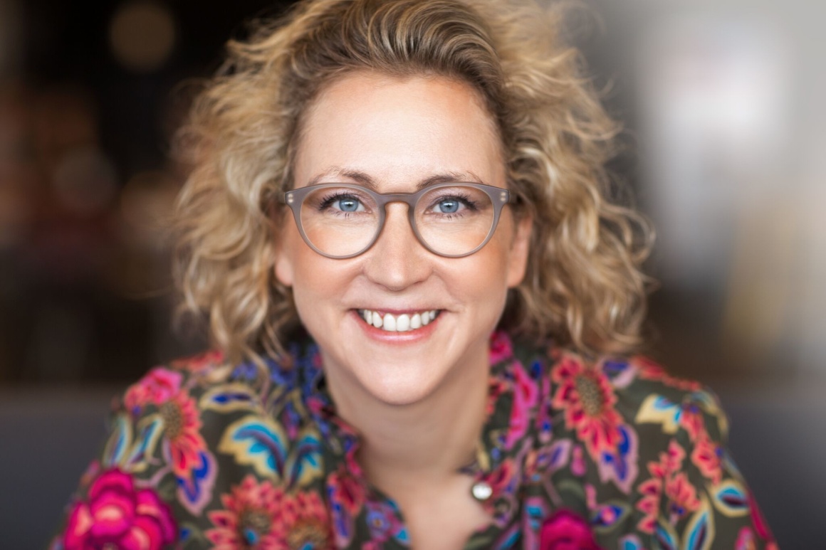 Woman with curly hair, glasses and colorful top smiles at camera...