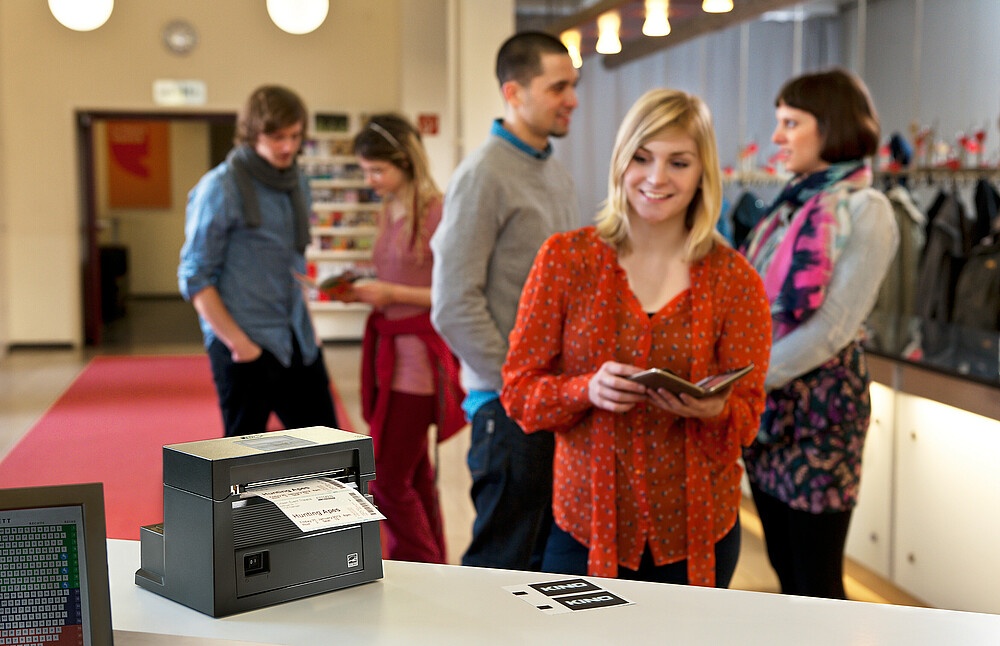 One person is standing in front of a counter with a printer, in the background...