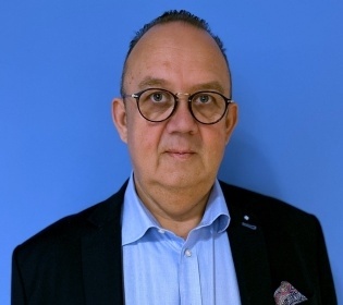 Man in light blue shirt and black jacket against blue background....