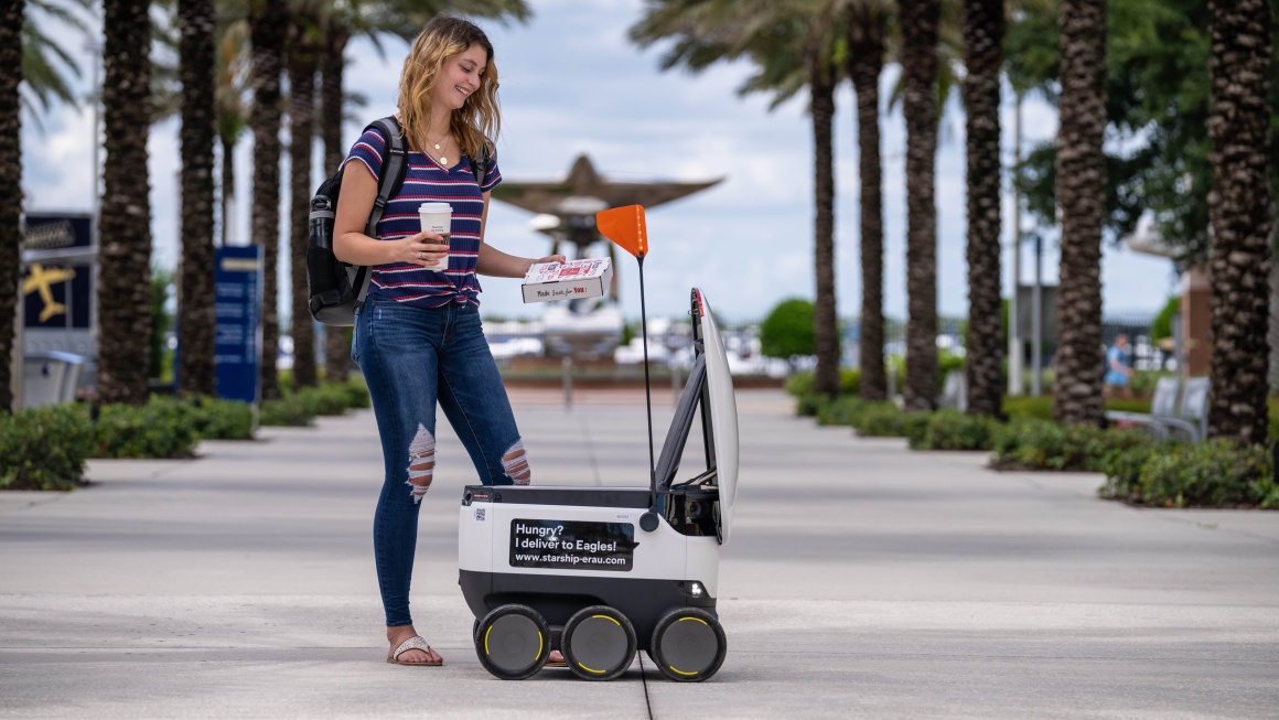 A person takes a pizza and a drink from a self-driving robot...