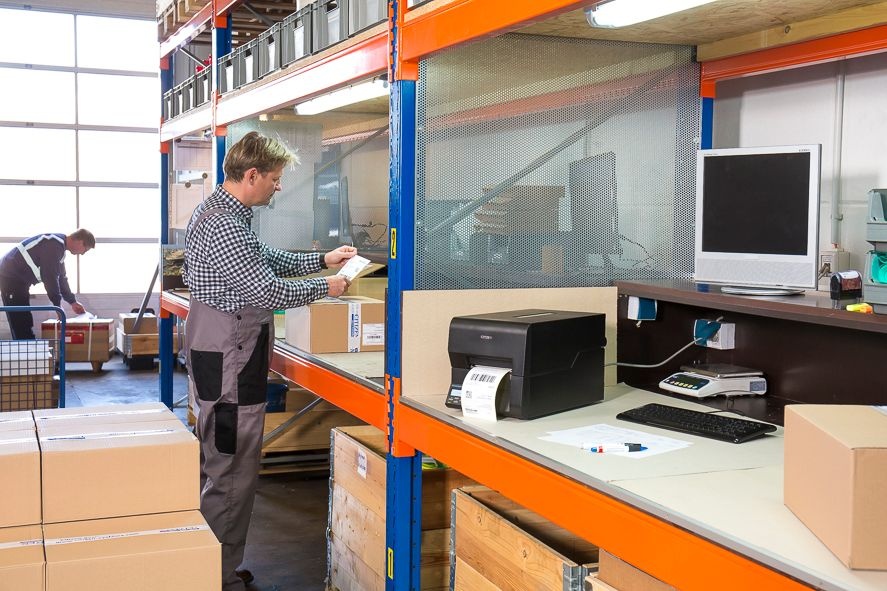 A label printer stands on a table, an employee can be seen in the background...