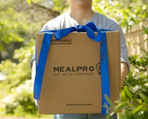 A person carries a cardboard box with the inscription Mealpro...