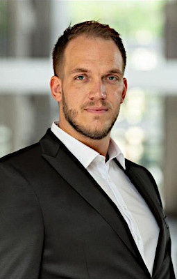 Man with short dark hair and three-day beard wears suit and looks into the...