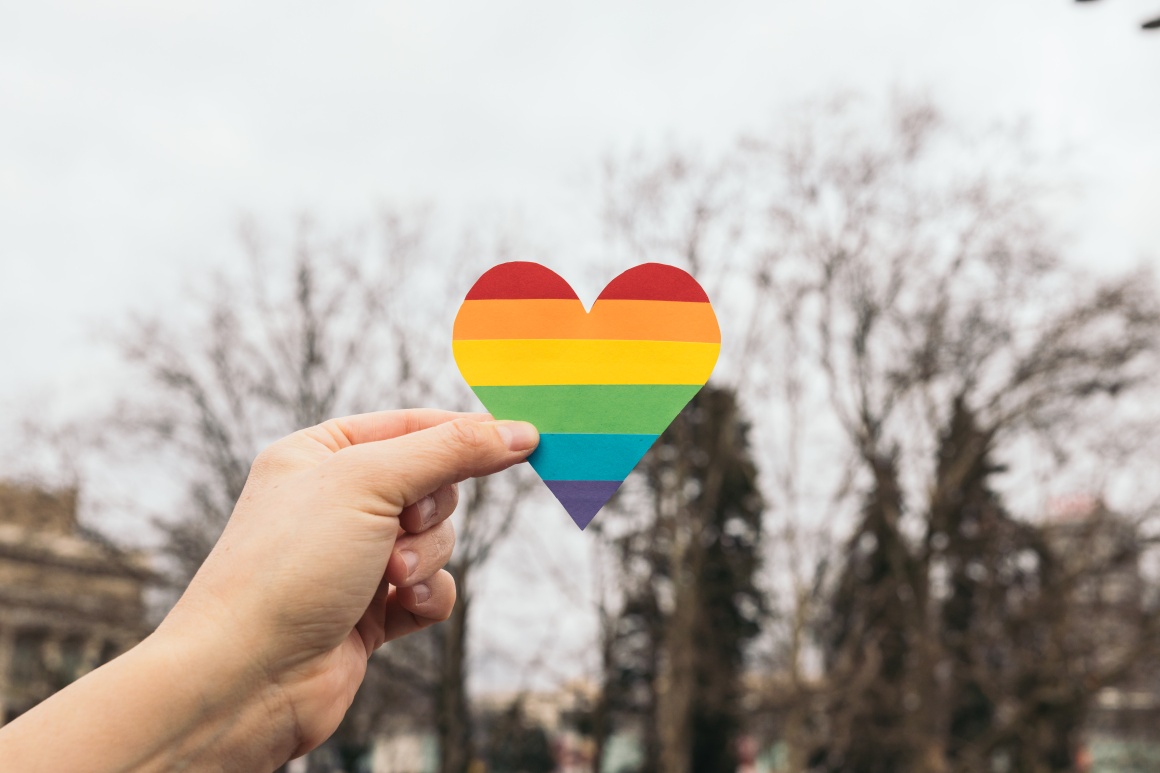 One hand holds a rainbow heart in the sky