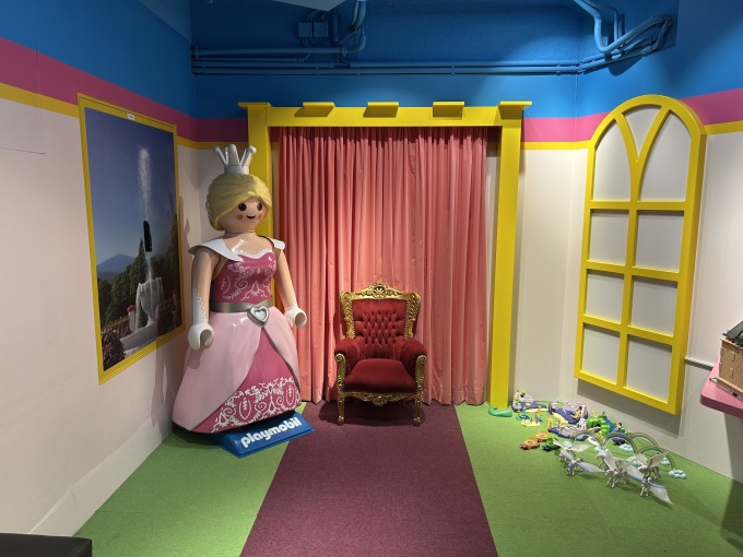 A room with a life-size figure of a queen, next to it a throne on which people...