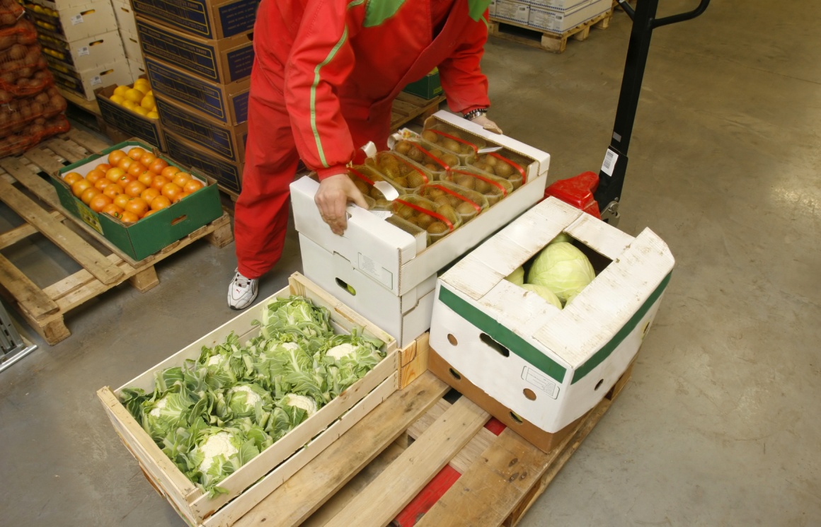 Photo: Bent employee lifts fruit box from wooden pallet; copyright:...