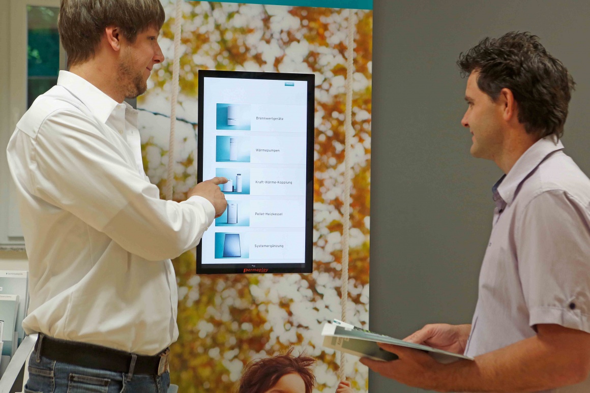 Photo: Two men in front of a digital information screen with products;...