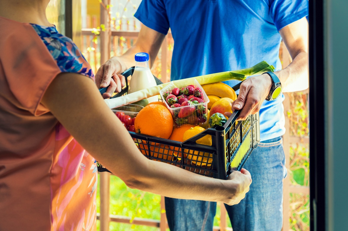 Delivery man hands over basket with groceries to woman at her door; copyright:...