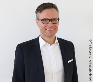 Man in a black suit and with glasses smiles into the camera...