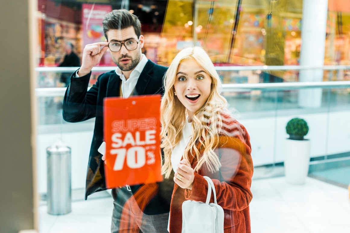 Man and woman look into a shop window with a sell sign....