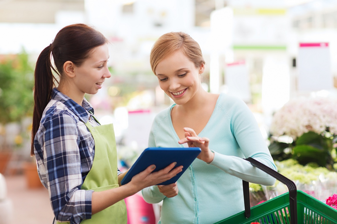 A saleswoman holds a tablet in her hand and advises a customer in a garden...