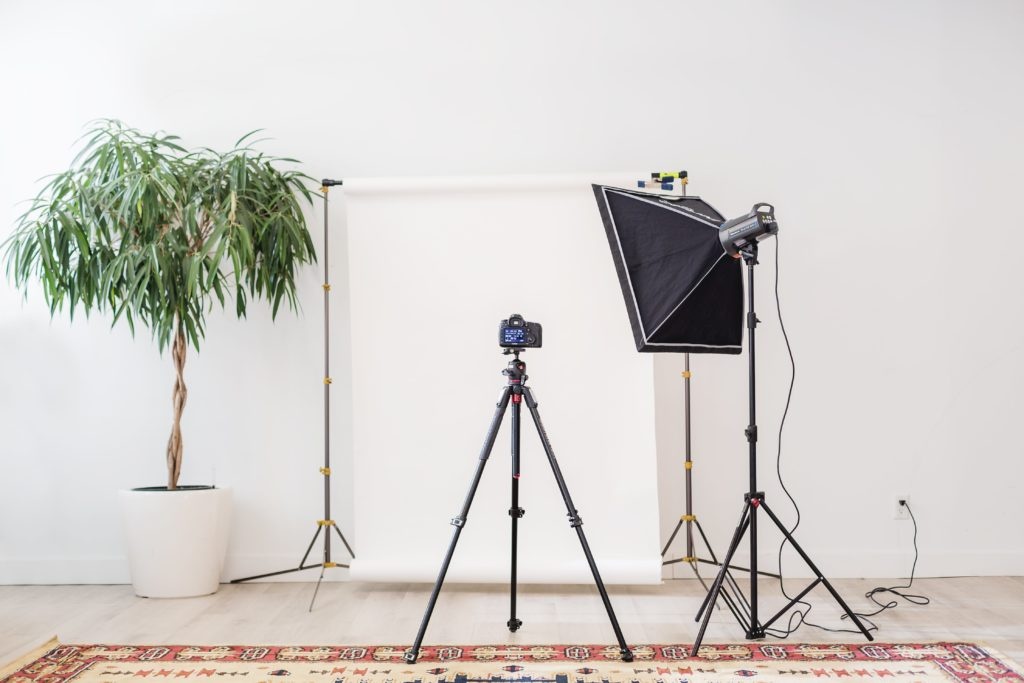 Camera tripod aimed at plants in front of a white wall....