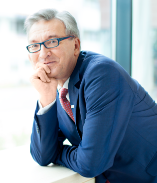 Man with glasses in blue suit smiles sideways into the camera....