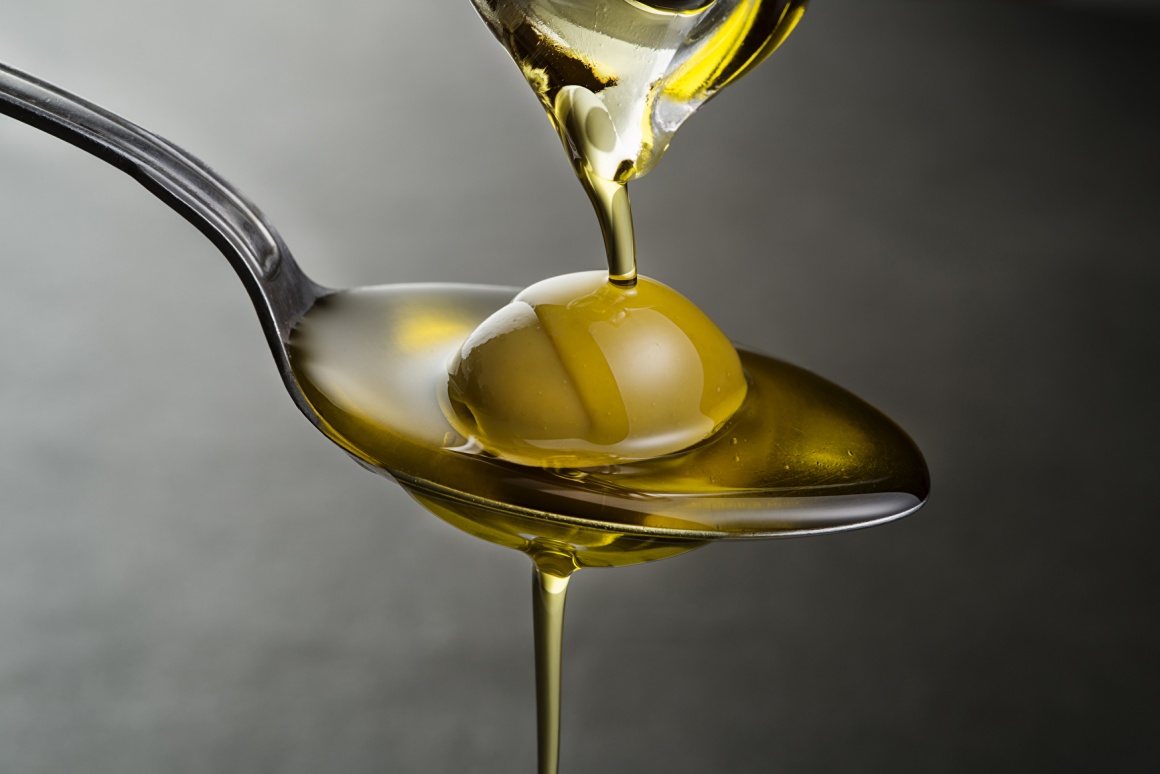 Olive oil trickling down onto a spoon with an olive on it; copyright:...