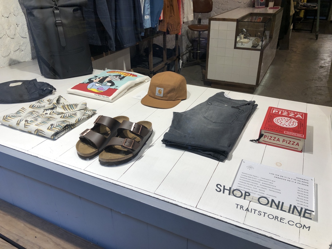 View through a shop window onto a simple white wooden counter with clothes;...