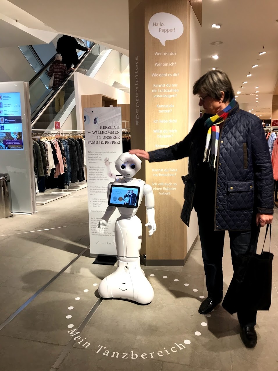 A customer in a fashion store strokes the white little robots head; copyright:...