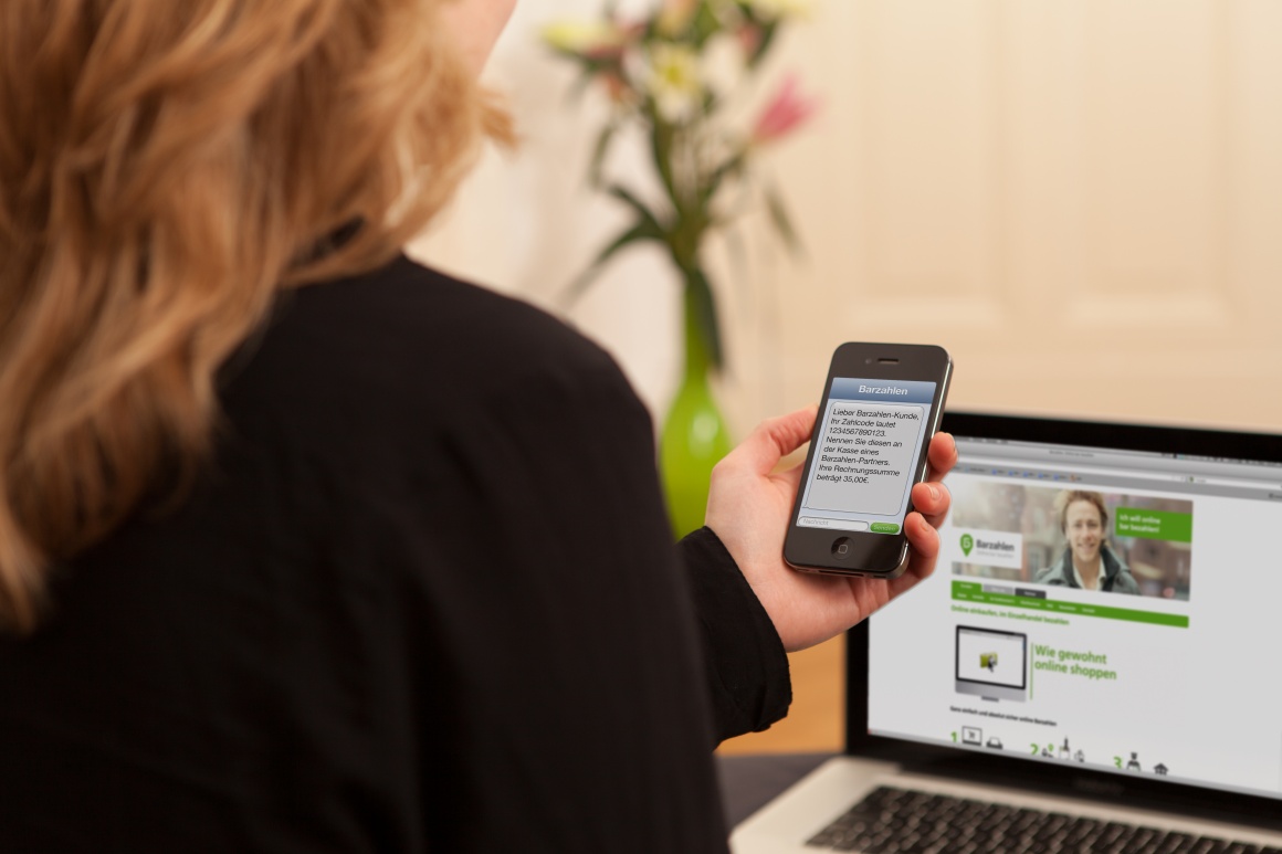 Blonde woman sitting in front of her laptop holding her smartphone in her hand...