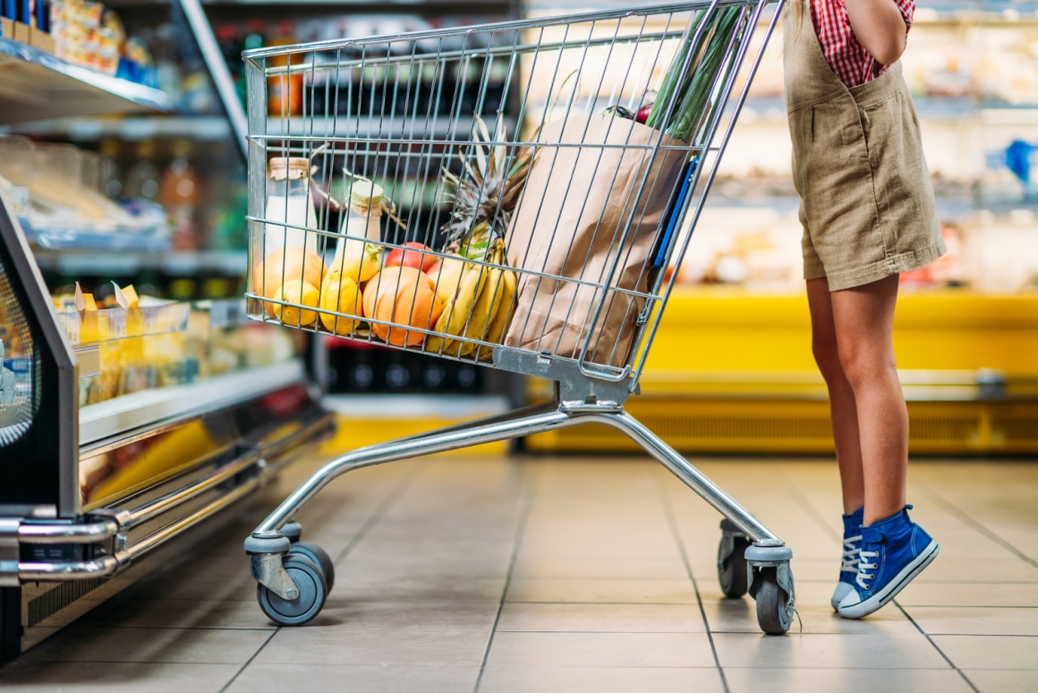 The feet of a child standing on tiptoes behind a shopping cart in a...