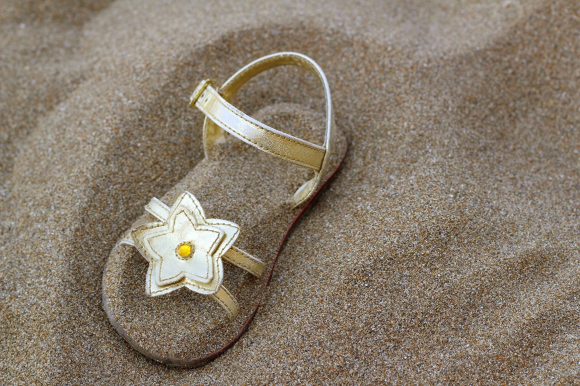 Sandal with a decorative flower half buried in sand; copyright: Bildagentur...