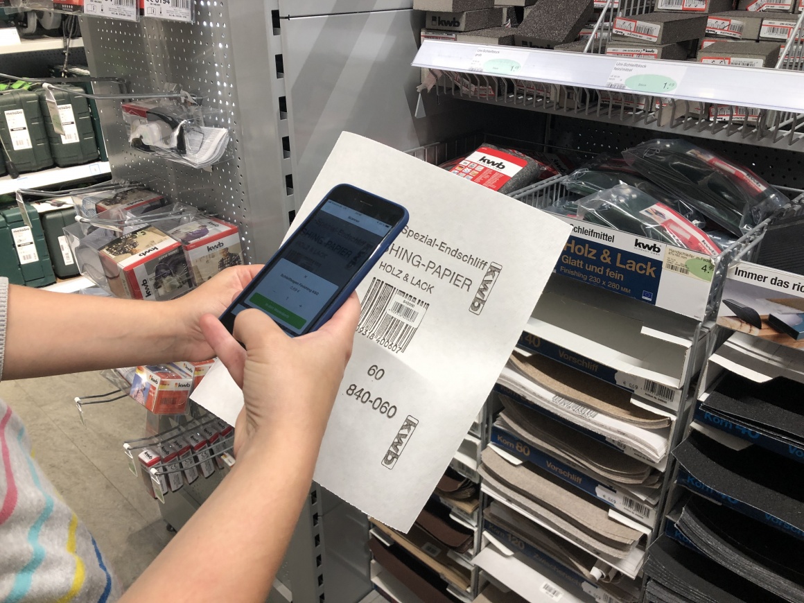 Person holding smartphone with camera in front of a paper with barcode;...