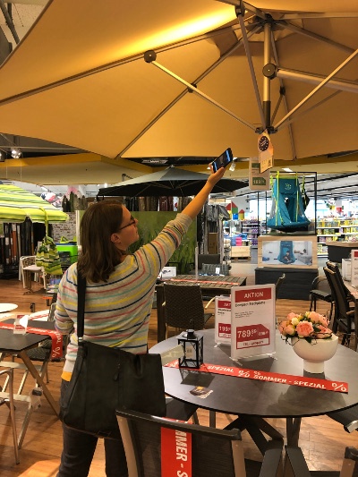 Person stretches out and holds smartphone up to the label on a parasol;...