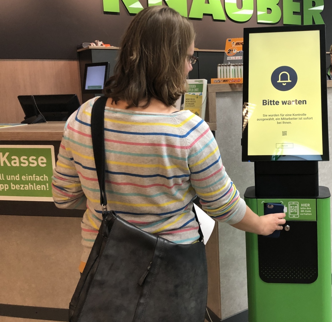 Woman holds smartphone to a digital stand in a store; copyright: iXtenso/Laska...