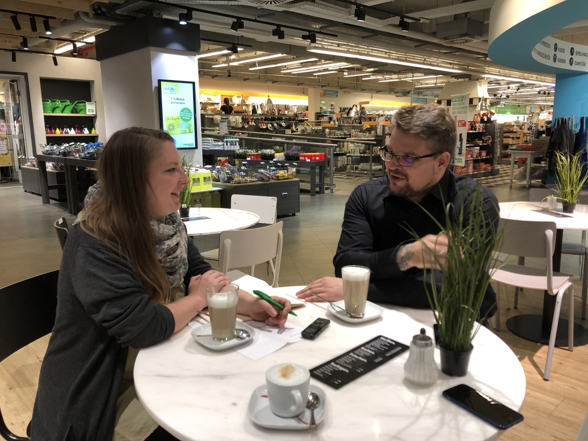 Left woman, right man - sitting at a table in the shop and talking....