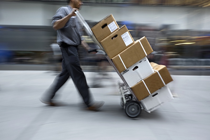 Man with sack truck loaded with parcels walks through a logistics center...