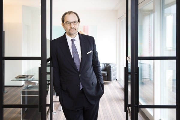 A man wearing a suit and tie is standing in the doorway to his office...