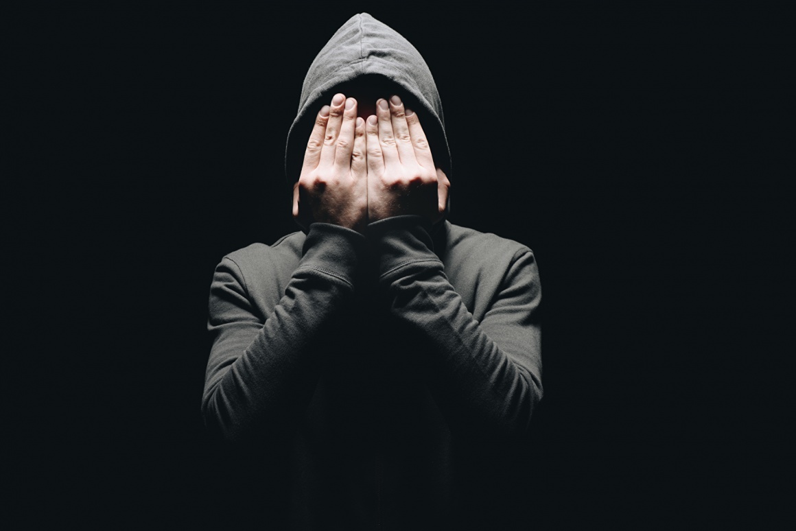 A person in a hoodie puts his hands in front of his face...
