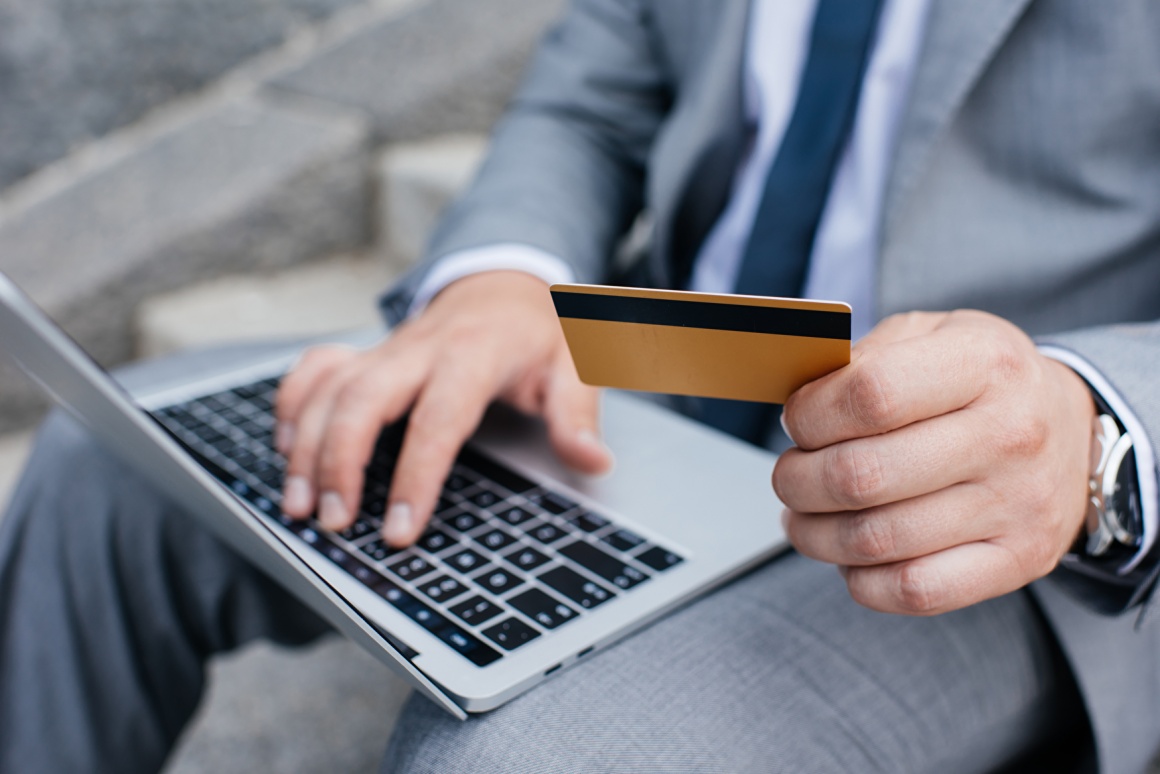 A man holding a laptop on his knees and a card in his hands...