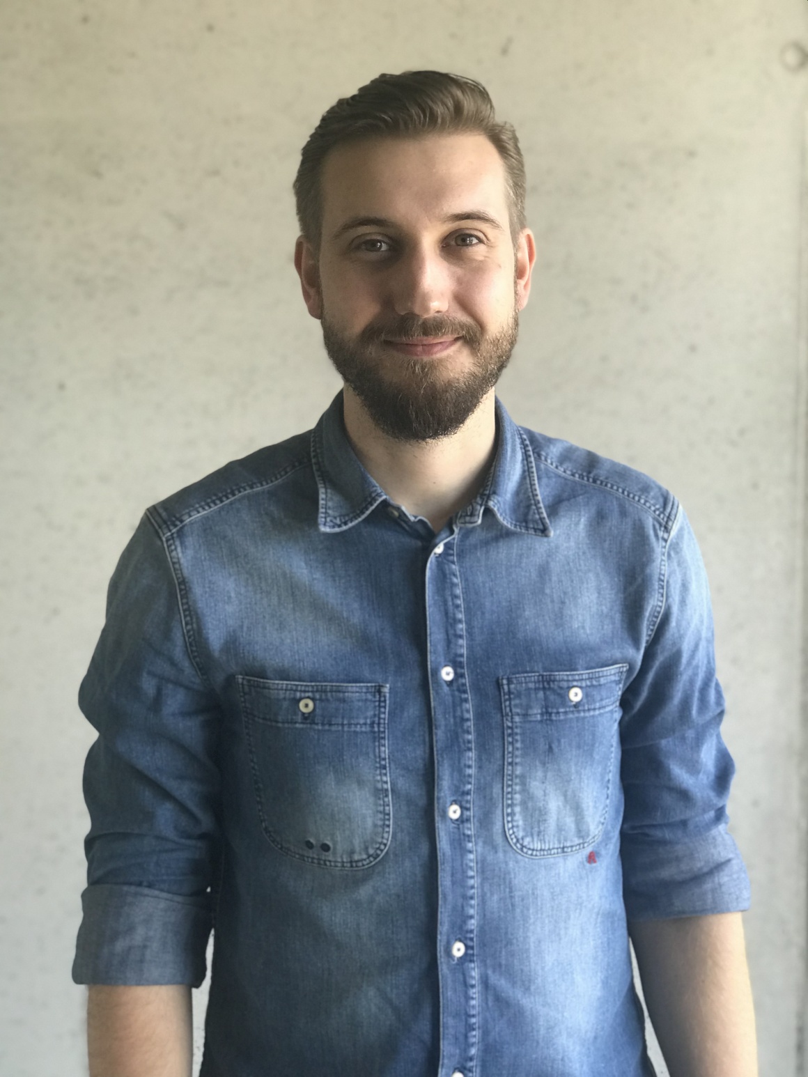 A young man in a denim shirt smiles into the camera...