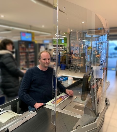 Employees of a supermarket sitting at the cash register behind a spit...